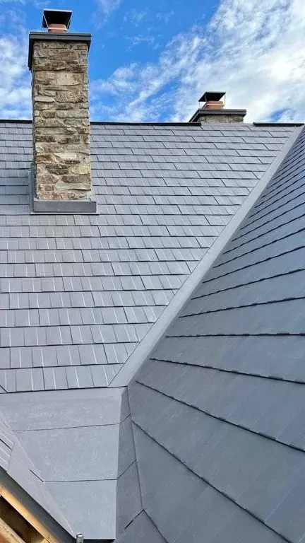 Toiture en tôle métallique grise avec cheminée en pierre, en cours d’installation